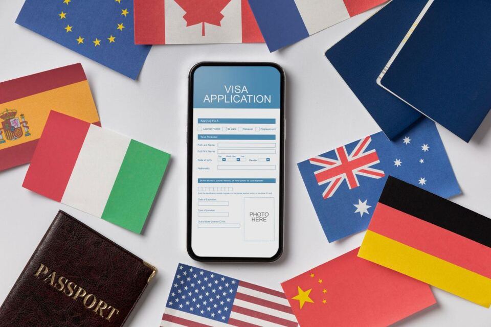 A phone showing a visa application form, surrounded by passports and the flags of several countries laid out on a white surface.