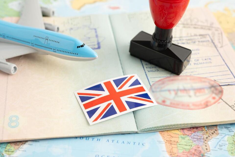 A toy aeroplane, a Union Jack sticker and a red rubber stamp resting on an open passport laid over a world map.